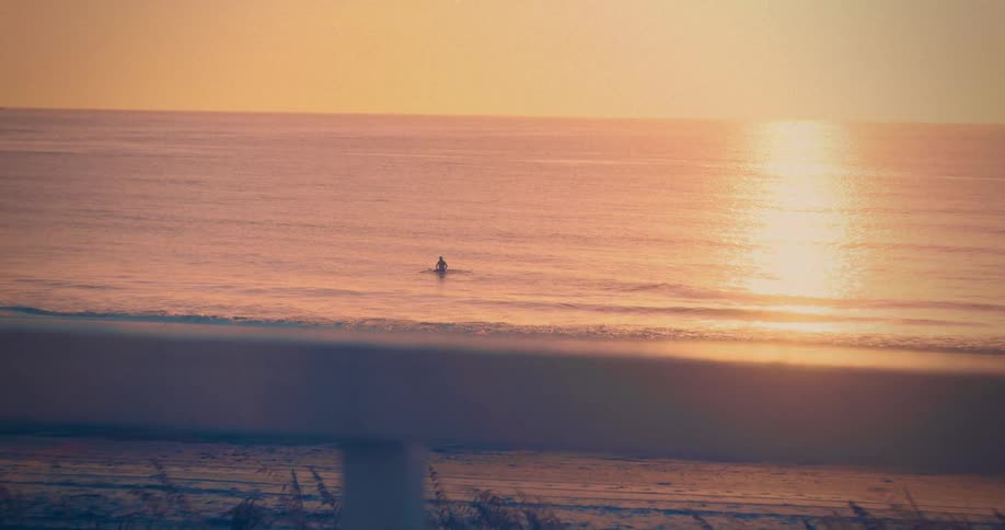 A person swims alone in the ocean at sunset as seen from the beach