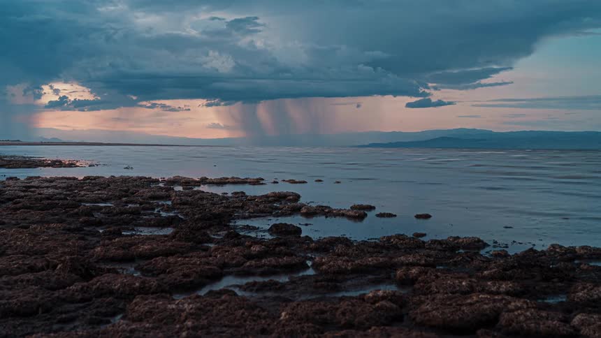 Distant rain falls over the sea beneath dark clouds at dusk