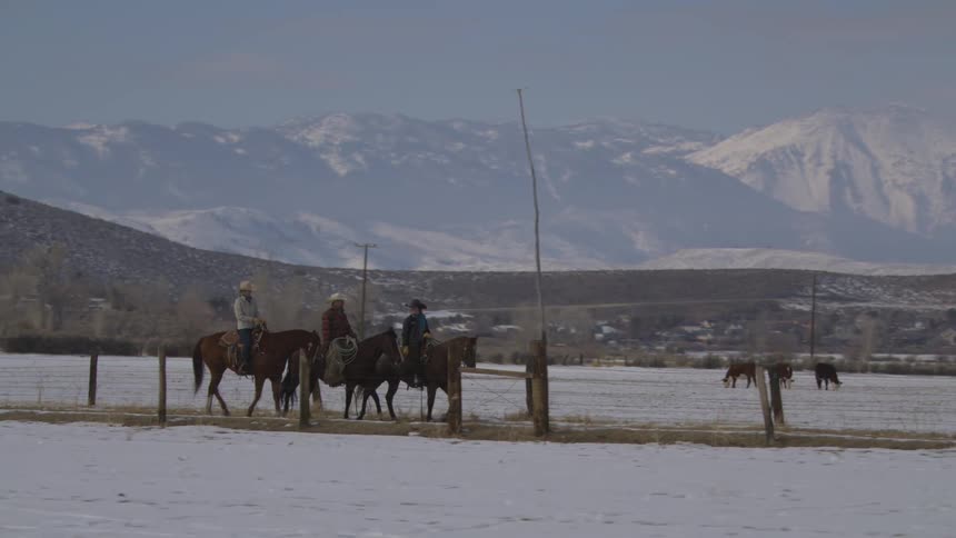 Riders cross a snowcovered field with snowcapped mountains in the background