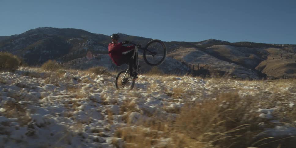Cyclist performing a wheelie on a trail surrounded by mountains
