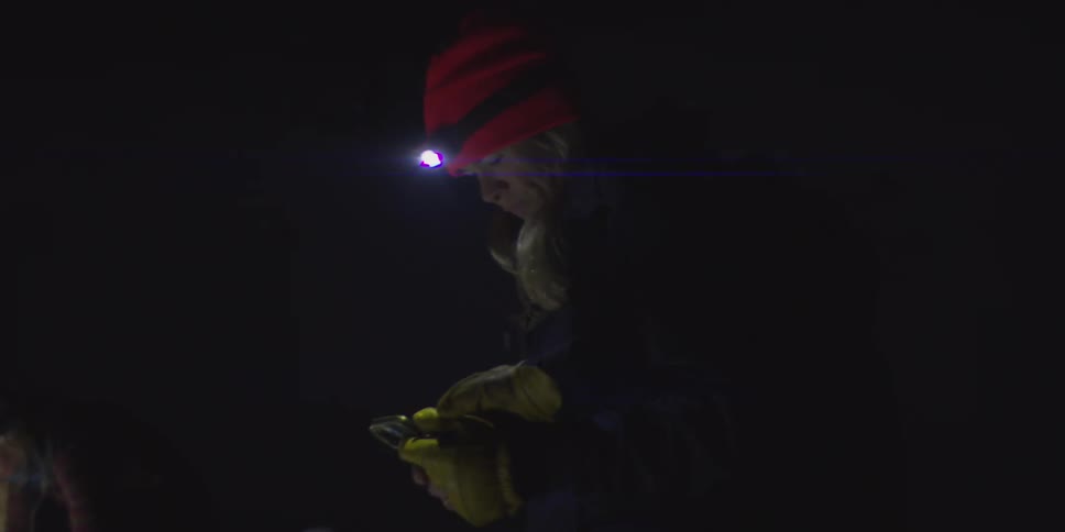 Two young women are outdoors at night wearing headlamps to light their way in the dark