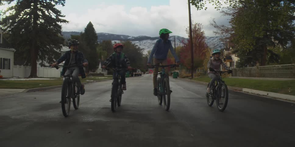 A group of kids is riding bikes down a street in a neighborhood