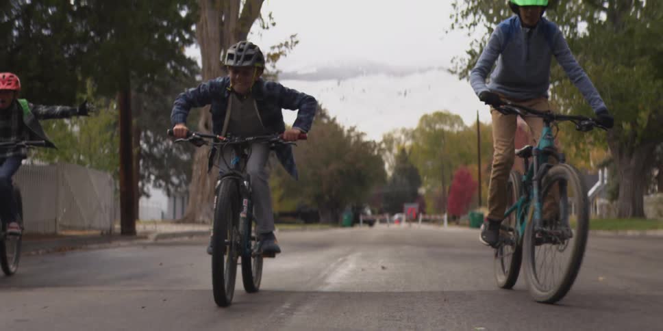 Four kids ride their bikes in the middle of the street at midday having fun together