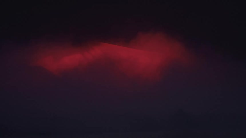 Person moves within a sheet under colored lighting during a performance on a dark foggy stage