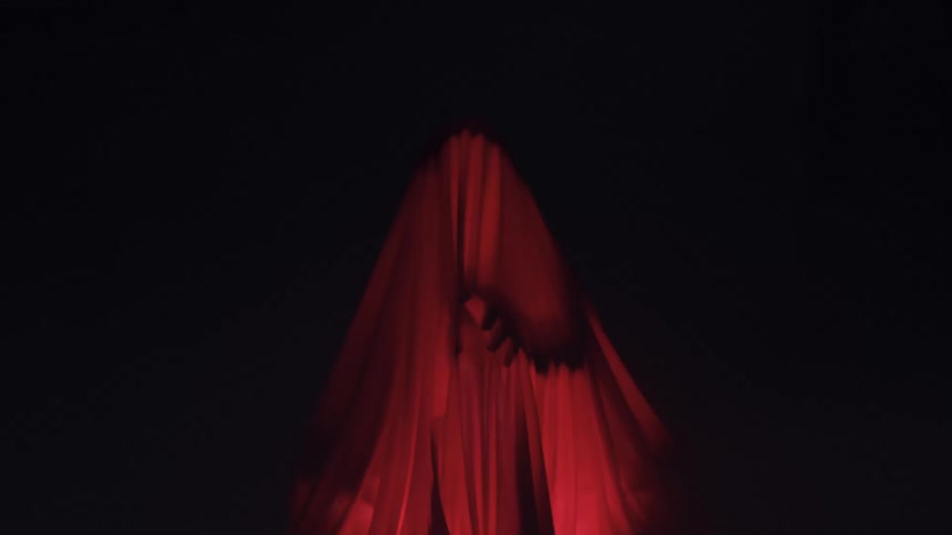 A figure reaches out in the dark under a sheet