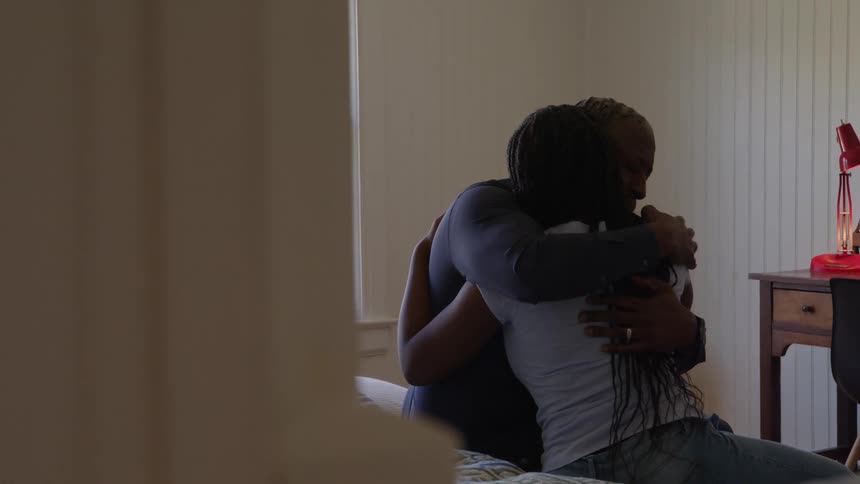 An older man and a young woman sitting on a bed with the man hugging and comforting her