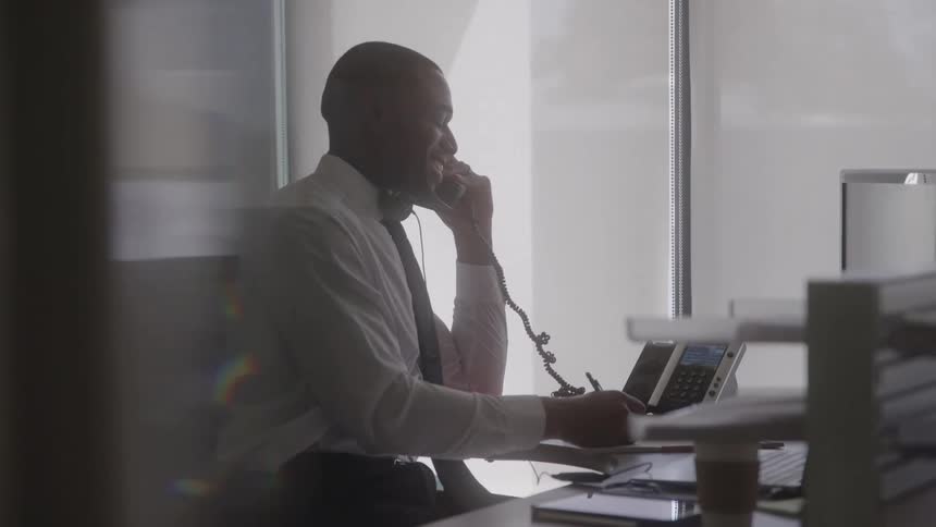 Office worker using his business phone smiles while taking notes