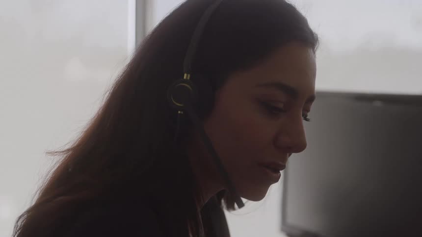 A female customer service agent talks on a headset in an office