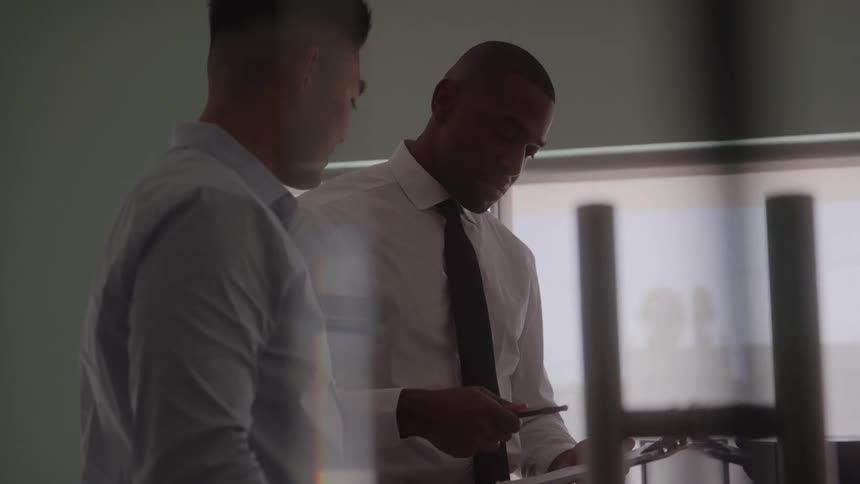 Two men in an office one of them showing a clipboard and saying something