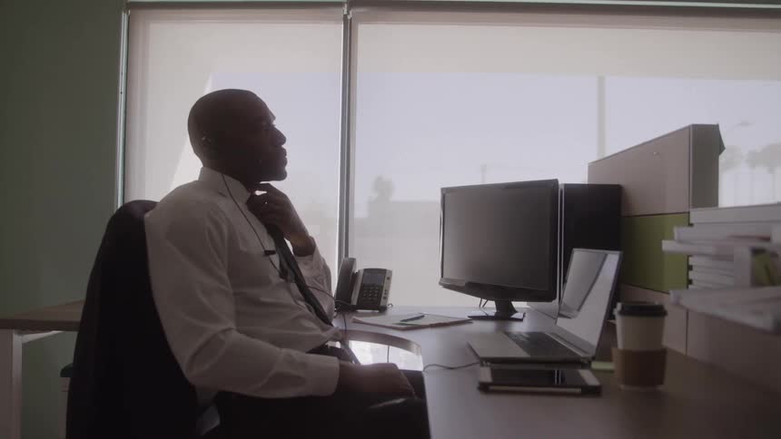 Man in a suit works on a laptop in an office lit by natural light