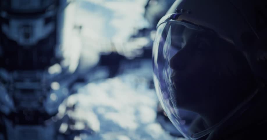 A dark close up profile shot of an astronaut, a sorf focus space station can be seen behind