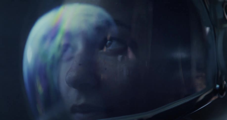 A woman in a space suit has a light shining on her helmet