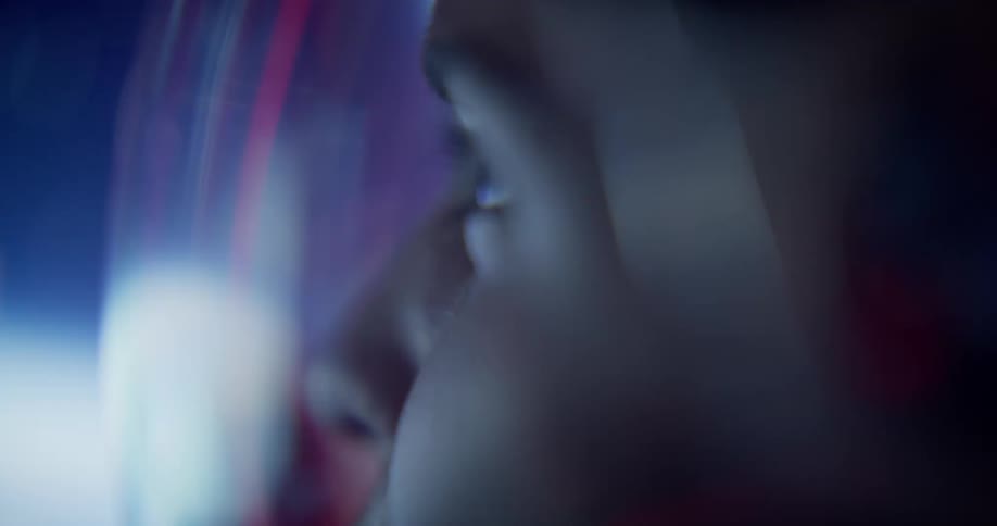 A woman in a space suit wipes her fingers on the glass as a red light flashes