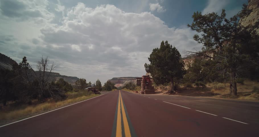 Paved road stretches between cliffs and vegetation under a cloudy sky