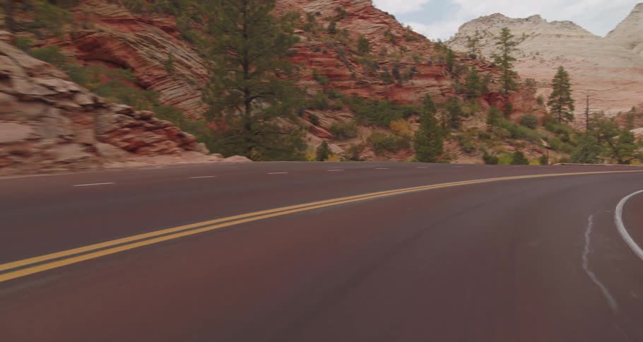 A winding road curves through rocky cliffs and pine trees in a desert mountain landscape