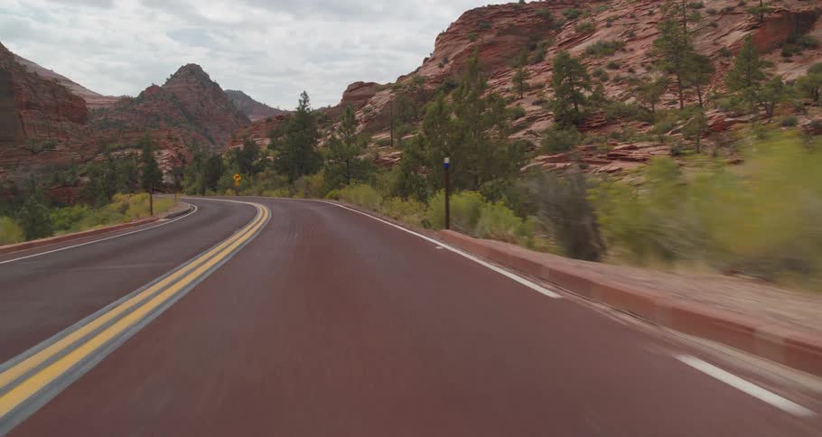 A winding road runs through curvy canyons and pine trees under a cloudy sky