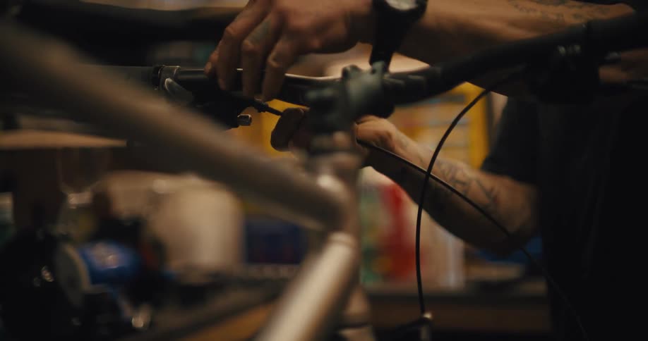 Close up of the handlebars of a bicycle as a mechanic works on the brake cable in a workshop
