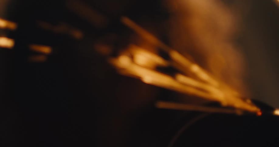 Close up focus pull from sparks to a woman wearing protective glasses operating an angle grinder