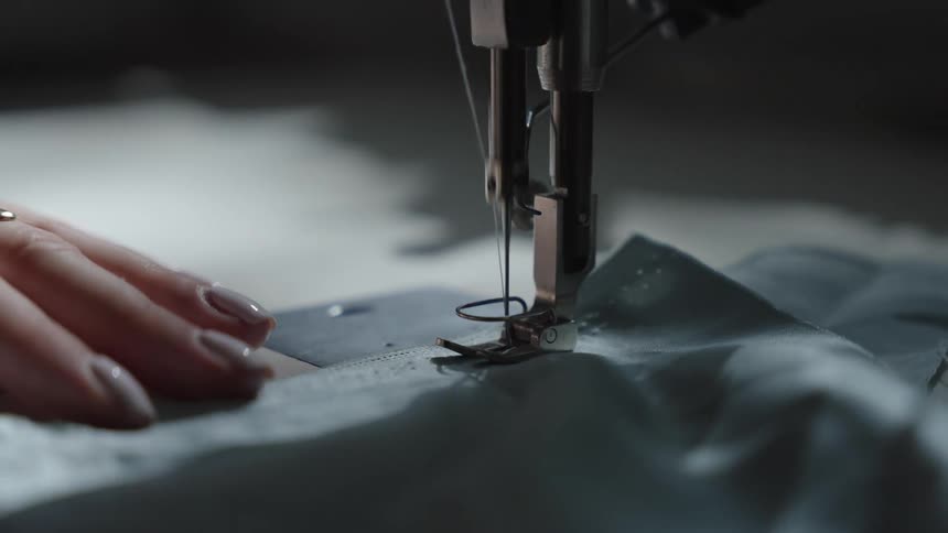 A woman sits behind a sewing machine sewing a piece of fabric