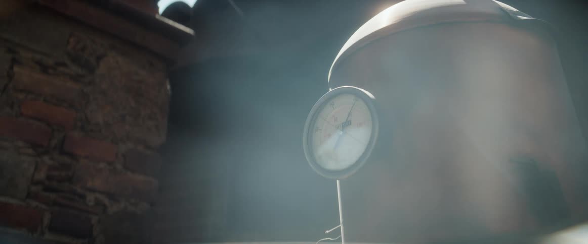 Steam blows around a pressure gauge placed on a covered pipe next to a brick chimney