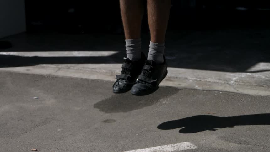 An athletes feet rhythmically jump over a skipping rope on an asphalt surface