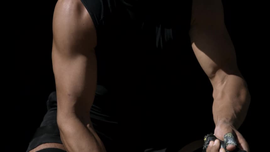 A person with muscular arms works battle ropes in a dark setting