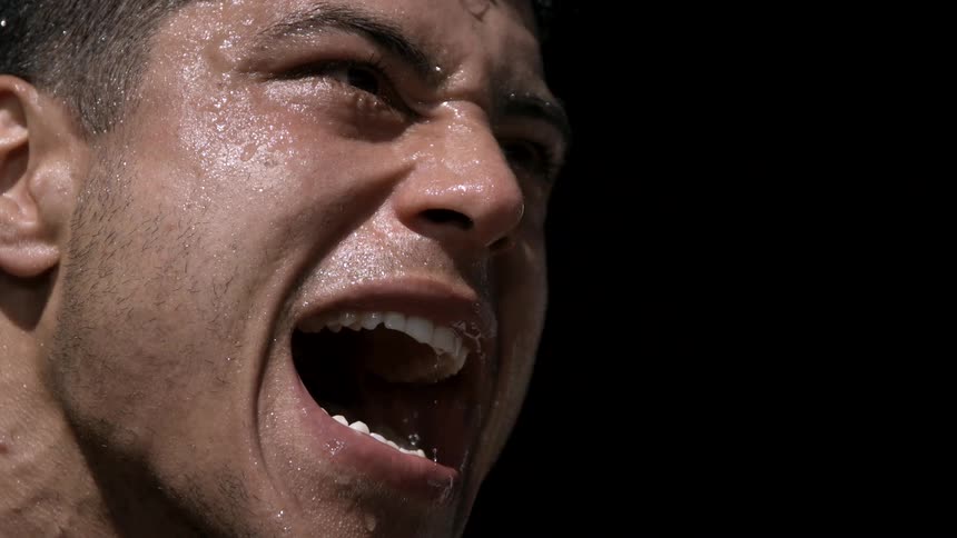 An intensely focused sweaty athlete yells with exertion as a bead of sweat drips from his lip