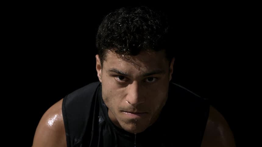 A sweaty man stares forward with intense focus as water drips from his face against a black background