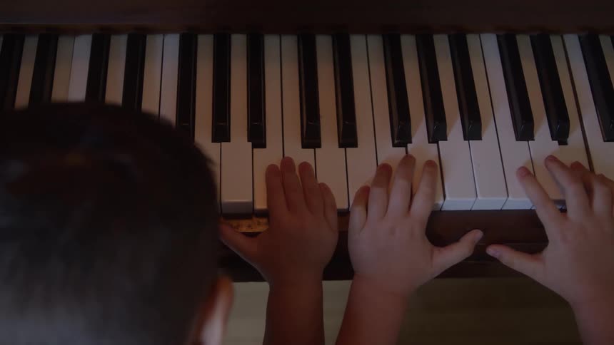 Closeup of a young childs hands playing piano keys indoors