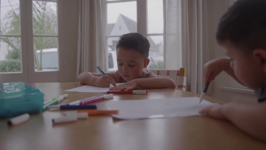 Siblings sit at the table at home and draw with markers