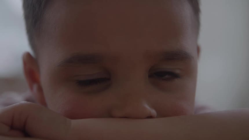 Young boy is leaning his face on his arm as he moves his eyes thinking