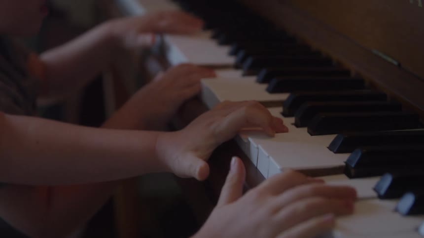 Closeup of two children playing piano keys together indoors
