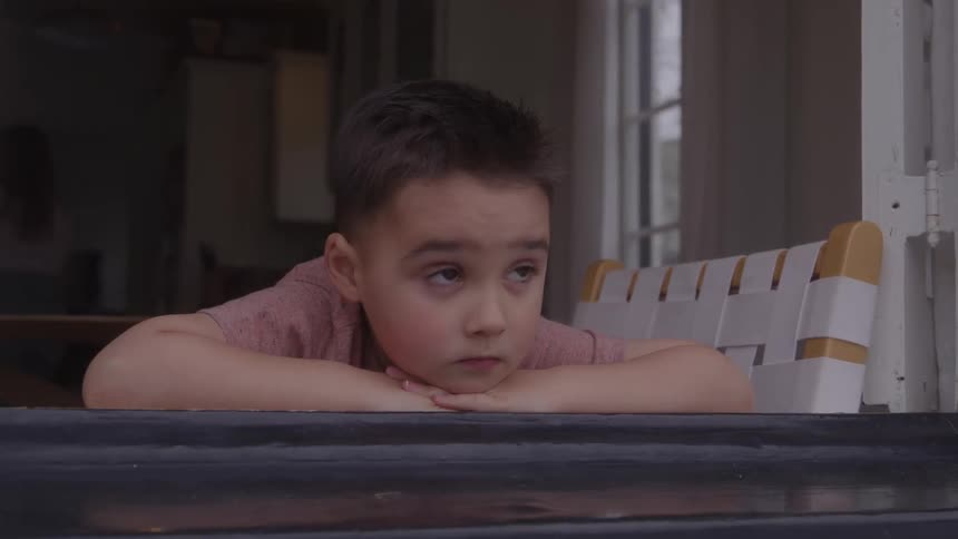 Boy rests his face on his hands while gazing thoughtfully out the window