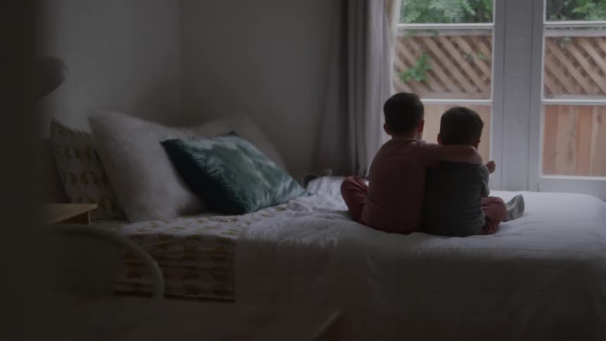 Children sitting on the bed look out the window on a cloudy morning