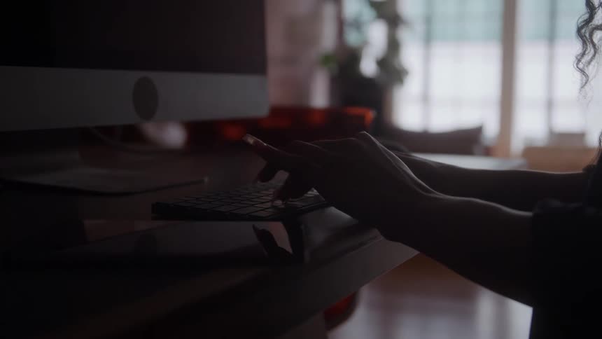 Hands type on a keyboard under soft light near a window
