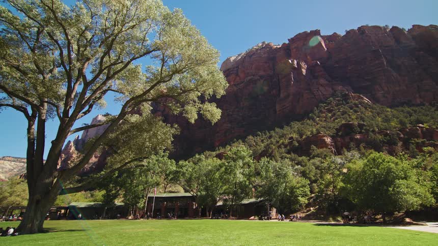 Grassy field with large trees is surrounded by red cliffs under a blue sky