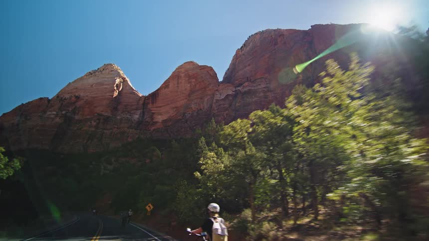 Cyclist rides along a road surrounded by reddish mountains at sunset