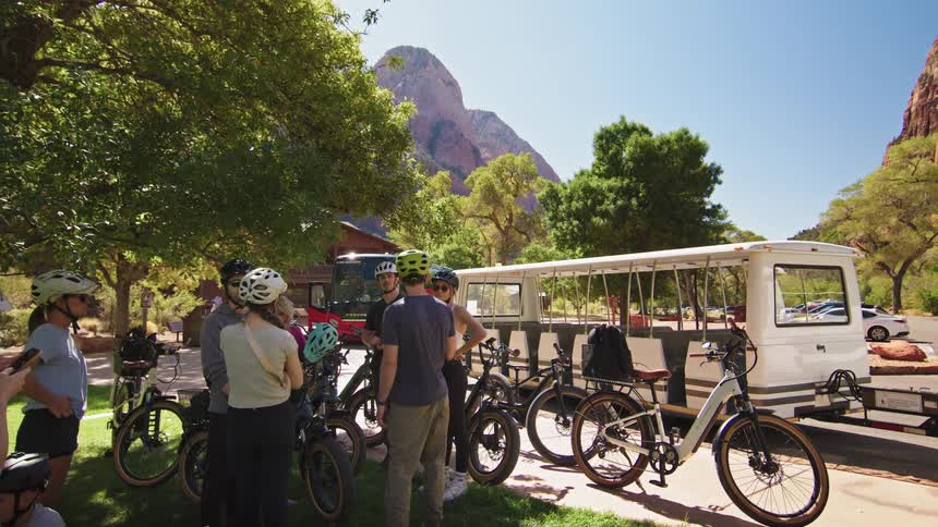 A group of cyclists gather near their bikes and a shuttle in a scenic canyon park