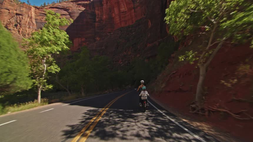 A woman and child ride on a bike on the trail by the mountain