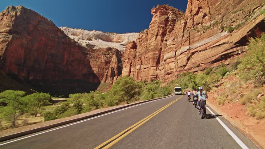 Group of people cycling on a mountain canyon road as a bus passes by