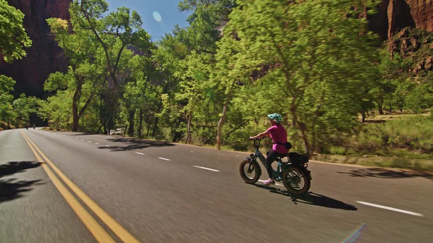 A woman is riding her bike on a highway that cuts through the mountains