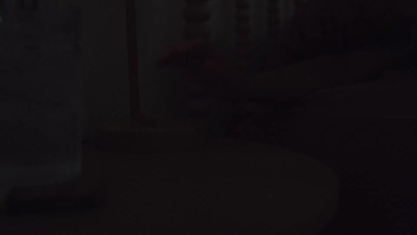 A persons hand reaches out to touch the wooden base of a small modern lamp on a nightstand instantly turning off the light to dark while pink blankets are visible in the background