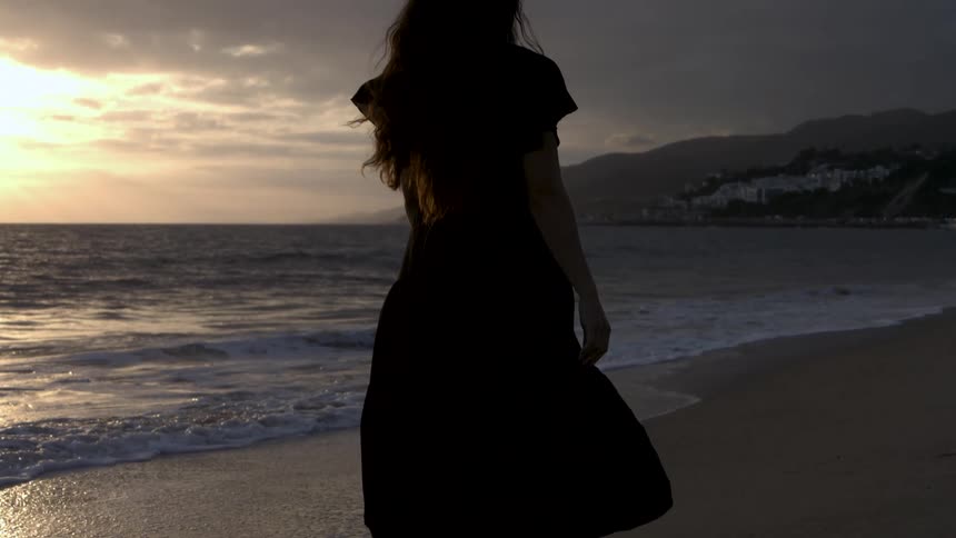 A woman walks along the coast at dusk