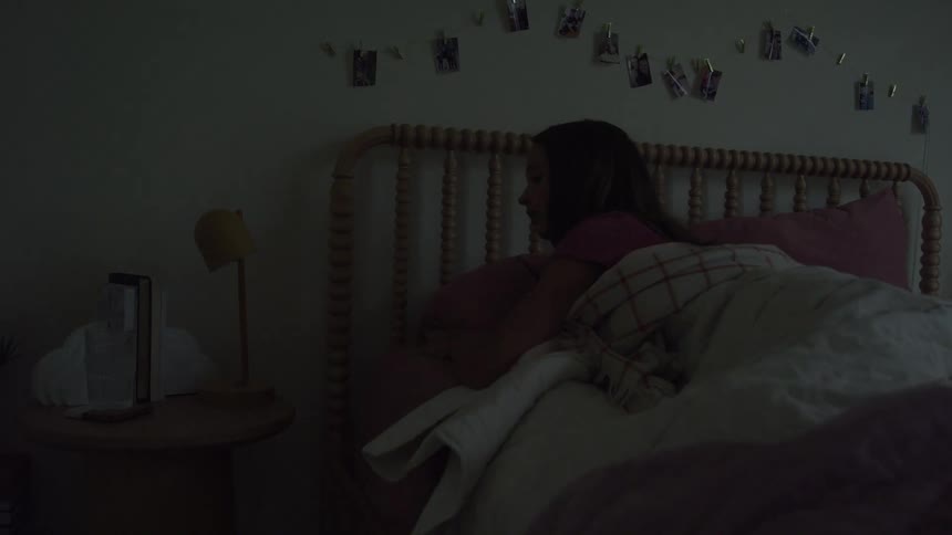 Girl turns off the bedside lamp and lies down to sleep in bed