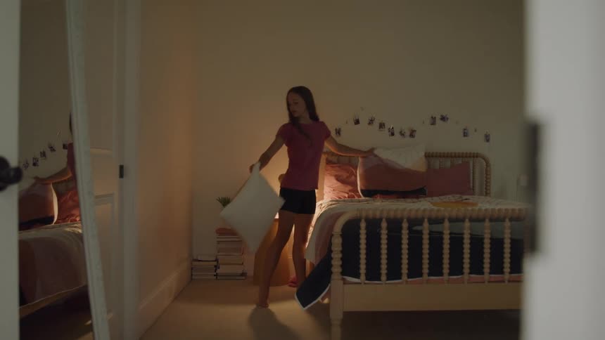 Girl makes her bed in a softly lit room before going to sleep