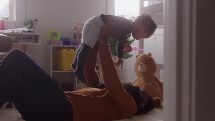 A father lies on his back lifting his son playfully in the air in a bright nursery