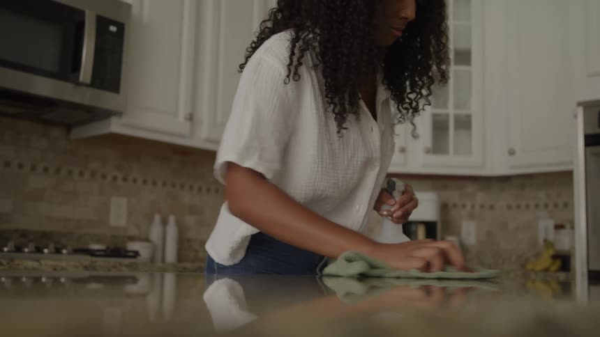 The woman is cleaning the counter with a rag