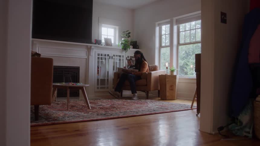 Young black man with a biracial toddler girl on his lap reading a book indoors during day time