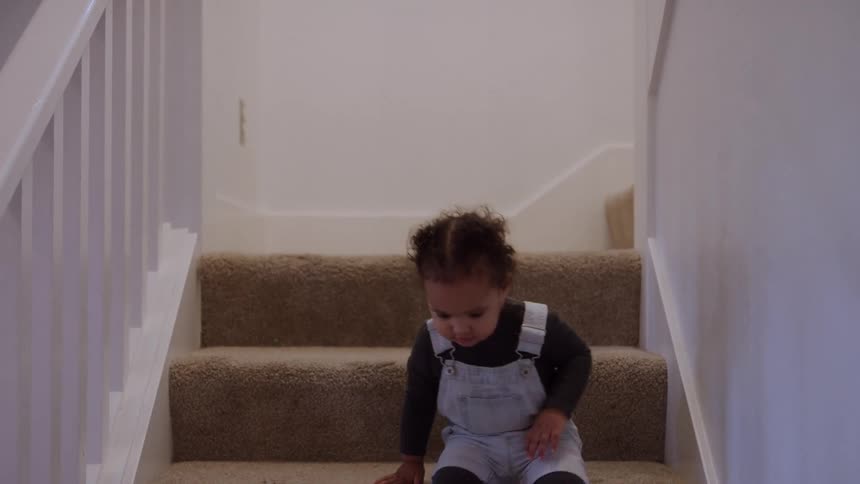 The video features a very young child dressed in denim overalls and a dark shirt carefully making their way down a carpeted staircasethe child descends stepbystep on their hands and knees concentrating on the movement as they eventually reach the