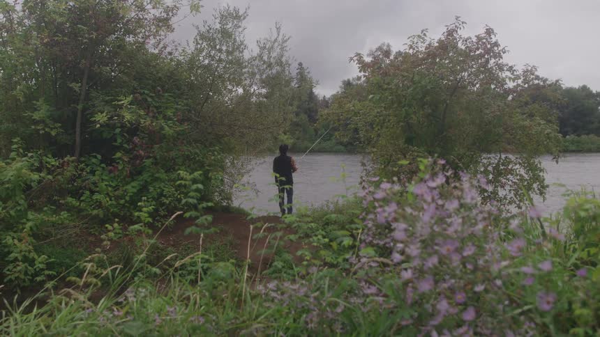 Man standing along the coast casts his line and holds his fishing pole
